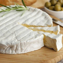 Load image into Gallery viewer, Brie cheese with 2 slices cut into it, herbs on top and olives in the background